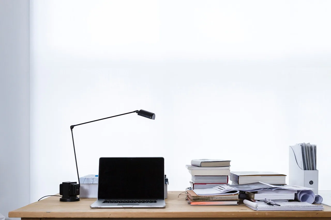 Bureau en bois avec une lampe, un ordinateur portable fermé et des livres